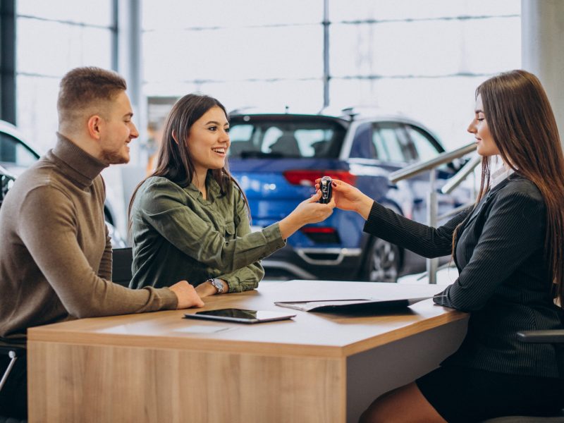 Young couple talking to a sales person in a car showroom